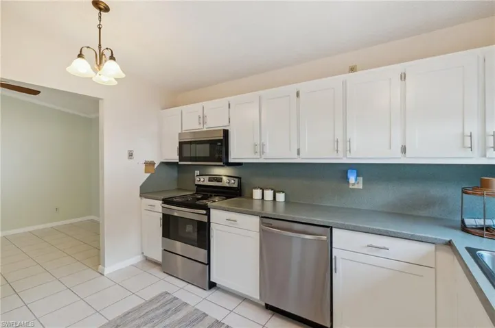 Kitchen featuring appliances with stainless steel finishes, pendant lighting, white cabinets, a chandelier, and light tile patterned floors