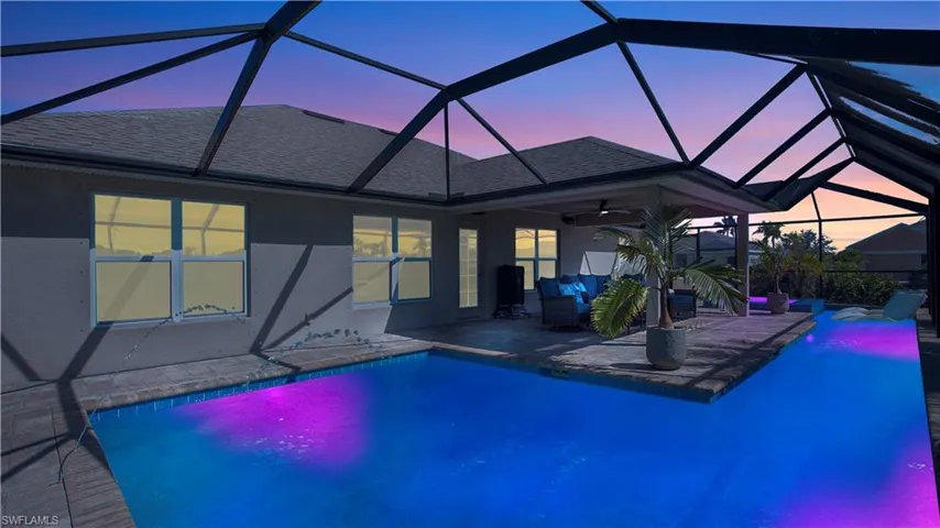 Pool at dusk featuring a patio, glass enclosure, and ceiling fan