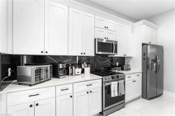 Kitchen with stainless steel appliances, white cabinetry, light stone countertops, decorative backsplash, and light marble finish flooring