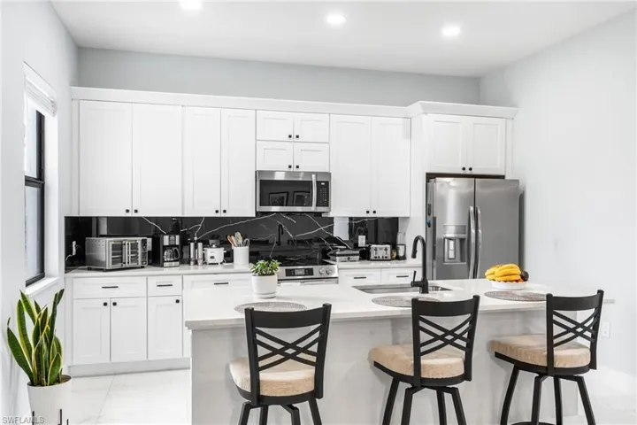 Kitchen featuring white cabinets, light stone countertops, stainless steel appliances, decorative backsplash, and recessed lighting