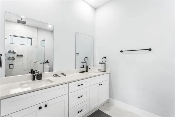 Full bath with a marble finish shower, double vanity, and light marble finish floors