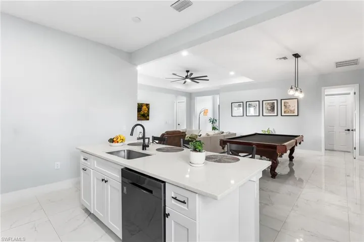Kitchen with billiards, a center island with sink, pendant lighting, dishwasher, and light marble finish floors