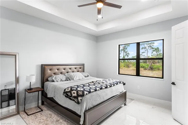 Bedroom with light marble finish floors, a tray ceiling, and ceiling fan