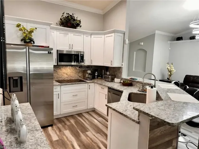 Kitchen with white cabinets, appliances with stainless steel finishes, light stone countertops, decorative backsplash, and ornamental molding