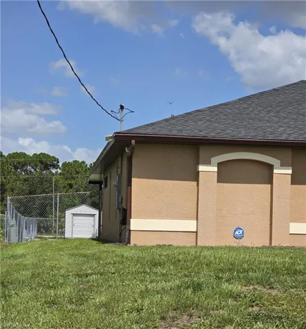 View of property exterior with stucco siding, roof with shingles, and an outdoor structure
