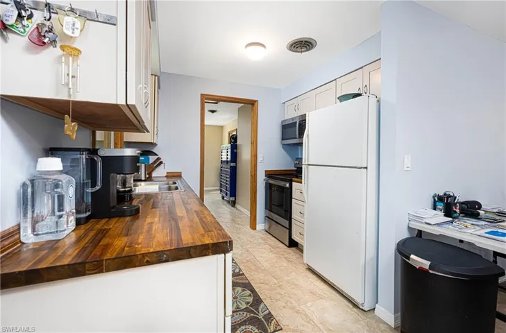 Kitchen with visible vents, wooden counters, stainless steel appliances, white cabinets, and baseboards