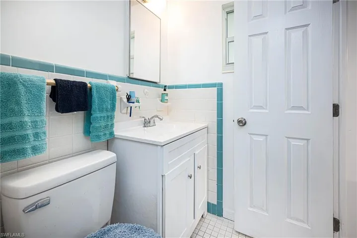 Bathroom featuring tile patterned flooring, toilet, vanity, wainscoting, and tile walls