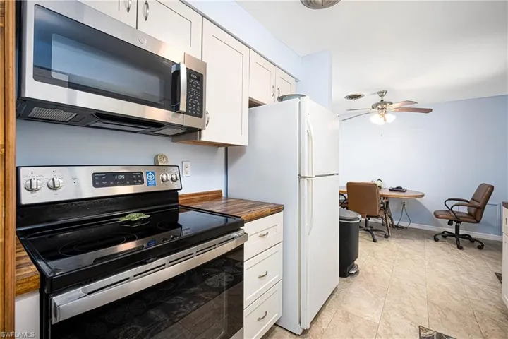 Kitchen featuring baseboards, ceiling fan, butcher block countertops, stainless steel appliances, and white cabinets