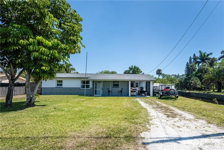 Ranch-style house with brick siding, a front lawn, fence, dirt driveway, and stucco siding