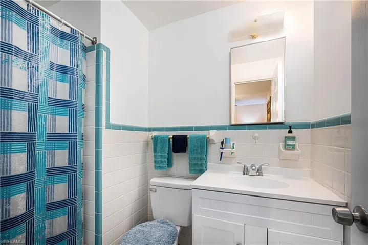Full bathroom with a wainscoted wall, toilet, vanity, a shower with curtain, and tile walls