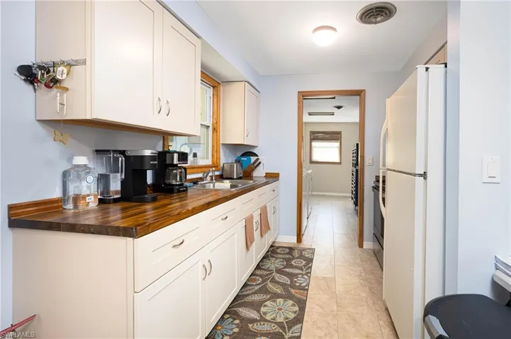 Kitchen featuring visible vents, butcher block counters, freestanding refrigerator, white cabinetry, and a sink