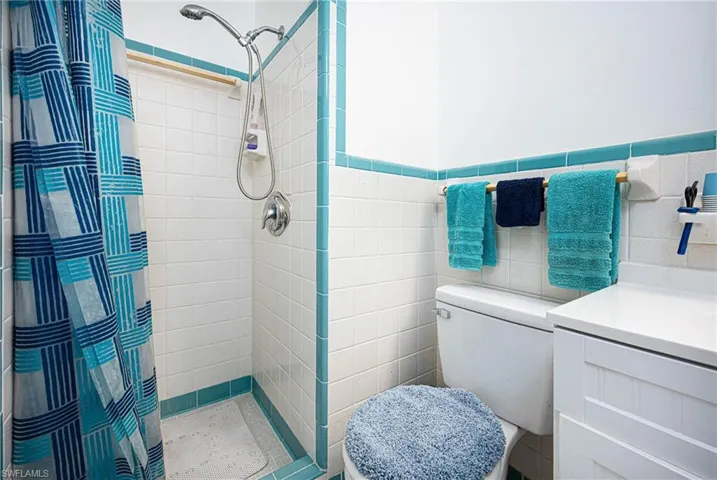 Bathroom featuring toilet, a stall shower, and tile walls