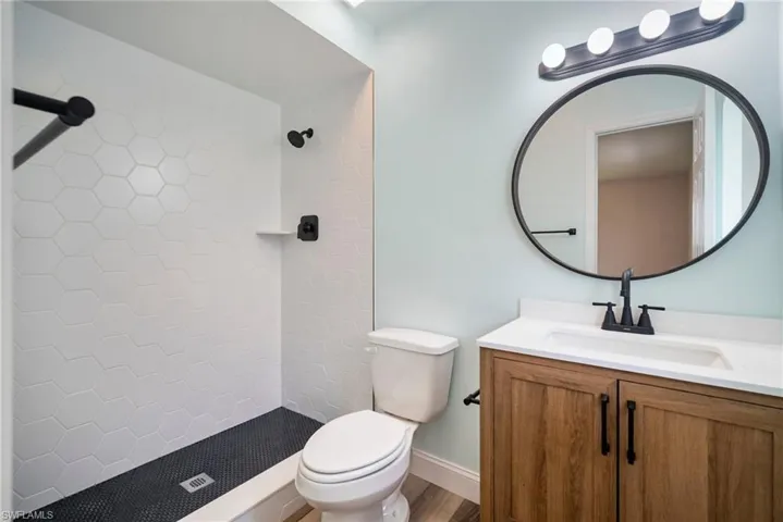 Bathroom with tiled shower, hardwood / wood-style floors, toilet, and vanity