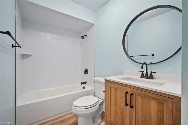 Full bathroom featuring vanity, tiled shower / bath combo, toilet, and wood-type flooring