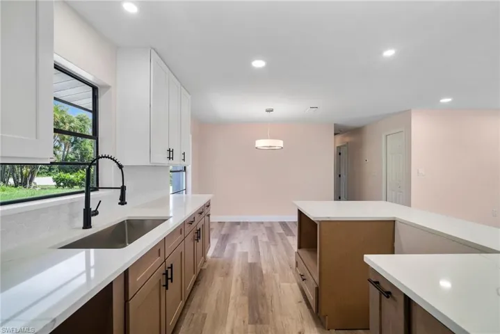 Kitchen featuring tasteful backsplash, sink, pendant lighting, light wood-type flooring, and white cabinetry