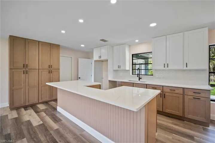 Kitchen with white cabinets, sink, light hardwood / wood-style floors, decorative backsplash, and a center island