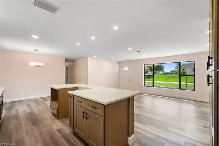 Kitchen with decorative light fixtures, light stone counters, light wood-type flooring, and a kitchen island