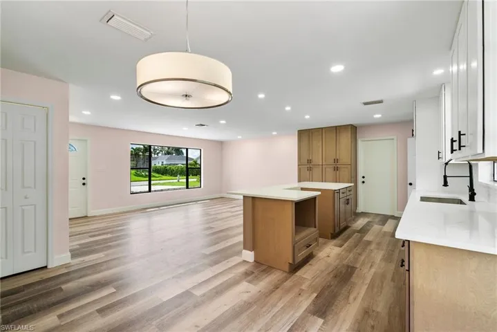Kitchen with white cabinetry, light hardwood / wood-style flooring, a kitchen island, pendant lighting, and sink