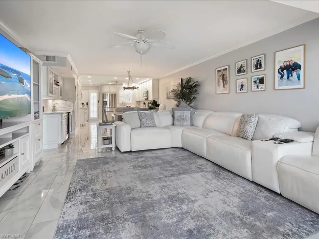 Living area featuring crown molding, light marble finish floors, a ceiling fan, and a chandelier