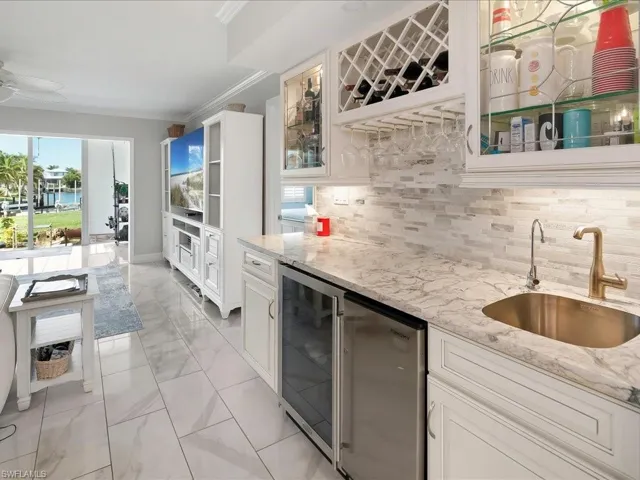 Indoor wet bar with white cabinetry, tasteful backsplash, light stone countertops, light marble finish floors, and beverage cooler