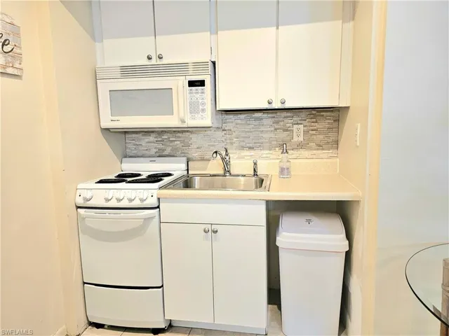 Kitchen with white appliances, white cabinets, backsplash, sink, and light tile floors
