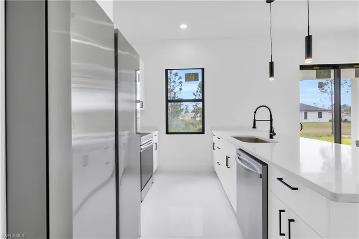 Kitchen with a peninsula, light stone countertops, pendant lighting, stainless steel appliances, and white cabinets