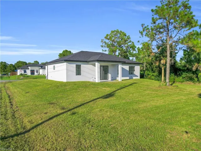 Rear view of house featuring a lawn, stucco siding, and a patio