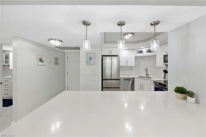 Kitchen with stainless steel appliances, white cabinetry, light countertops, decorative backsplash, and pendant lighting
