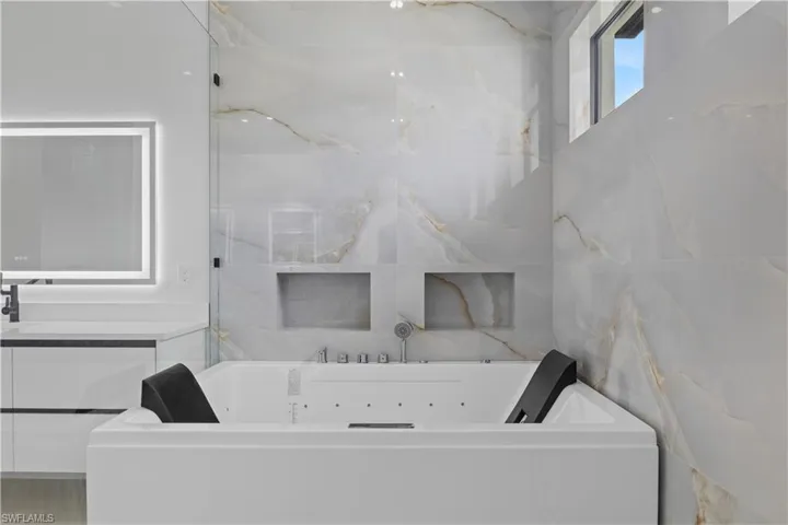 Full bathroom featuring vanity, a tub with jets, and tile walls
