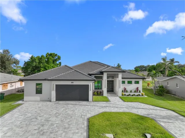 Prairie-style home with a garage, decorative driveway, a front lawn, stucco siding, and a tiled roof