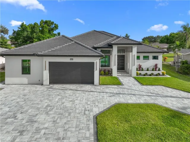 View of front of house featuring an attached garage, decorative driveway, a front lawn, stucco siding, and a tile roof