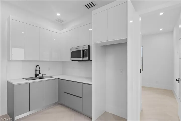 Kitchen featuring modern cabinets, stainless steel microwave, white cabinets, gray cabinets, and recessed lighting