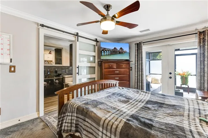 Bedroom featuring a barn door, ornamental molding, access to exterior, french doors, and a ceiling fan