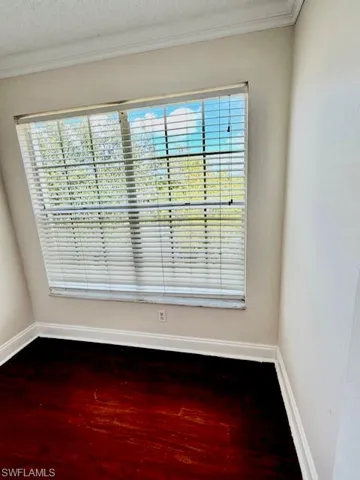 Unfurnished room with dark wood-type flooring, ornamental molding, healthy amount of natural light, and a textured ceiling