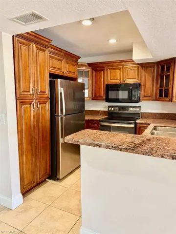 Kitchen featuring glass fronted cabinets, a textured ceiling, freestanding refrigerator, range with electric cooktop, and black microwave