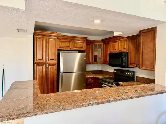 Kitchen with black appliances, light stone countertops, glass fronted cabinets, a peninsula, and a textured ceiling