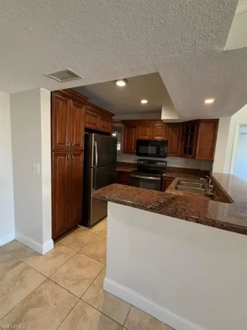 Kitchen with electric stove, a peninsula, a textured ceiling, freestanding refrigerator, and black microwave