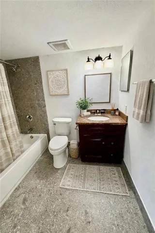 Full bathroom featuring vanity, shower / bath combo, a textured ceiling, and a textured wall