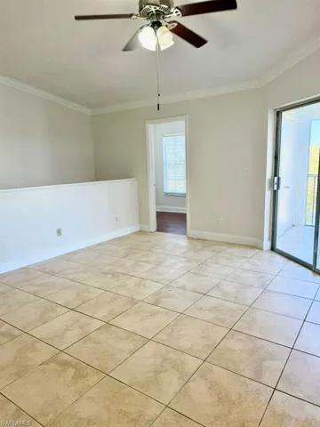 Empty room with a ceiling fan, crown molding, and light tile patterned floors