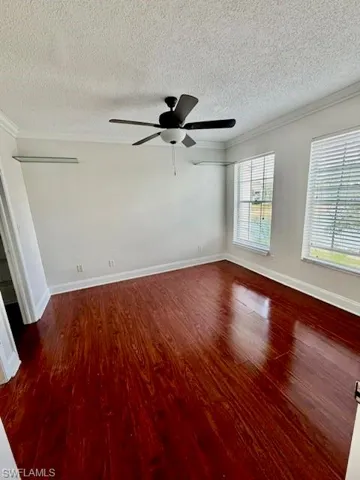 Empty room with crown molding, dark wood-style floors, a textured ceiling, and ceiling fan