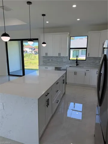 Kitchen with light marble finish flooring, fridge, light stone countertops, backsplash, and white cabinetry