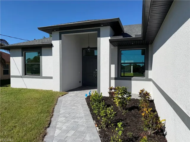Doorway to property featuring a lawn, stucco siding, and a shingled roof