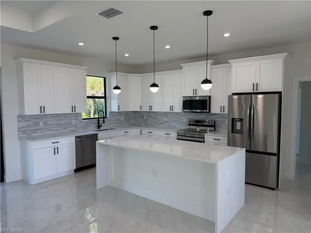 Kitchen with appliances with stainless steel finishes, a kitchen island, backsplash, light stone counters, and recessed lighting