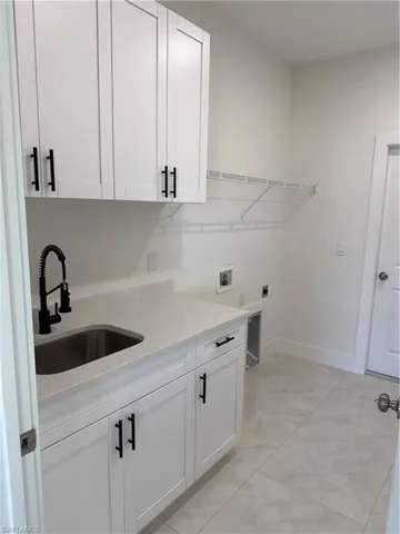 Washroom with hookup for a washing machine, cabinet space, light tile patterned floors, and electric dryer hookup