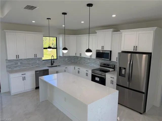 Kitchen featuring appliances with stainless steel finishes, a center island, white cabinetry, light stone countertops, and decorative backsplash