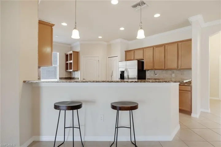 Kitchen featuring stainless steel fridge with ice dispenser, decorative backsplash, light tile patterned floors, kitchen peninsula, and crown molding