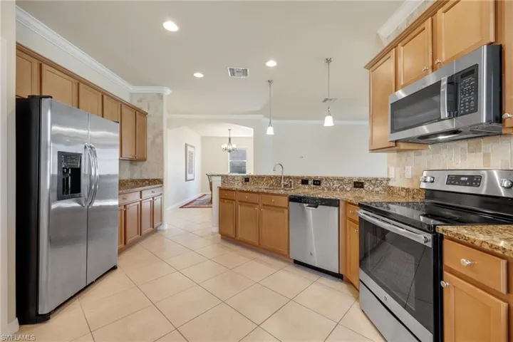 Kitchen featuring appliances with stainless steel finishes, sink, backsplash, hanging light fixtures, and ornamental molding