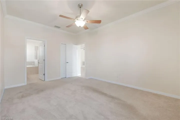 Unfurnished bedroom with crown molding, ensuite bath, light carpet, a closet, and ceiling fan