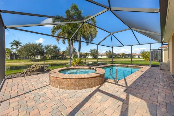 View of pool with an in ground hot tub, a water view, glass enclosure, and a patio