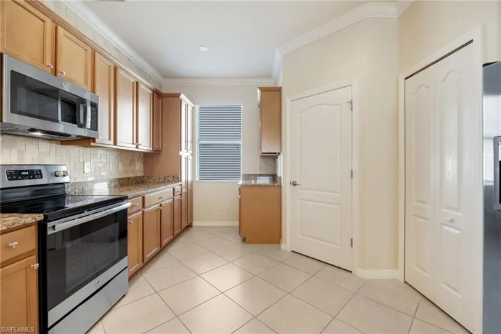 Kitchen featuring backsplash, light tile patterned floors, light stone counters, stainless steel appliances, and crown molding